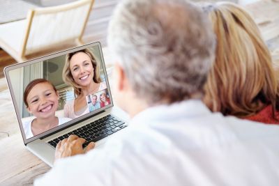 View over the shoulder of a senior man & woman on a laptop playing Zoom games with family