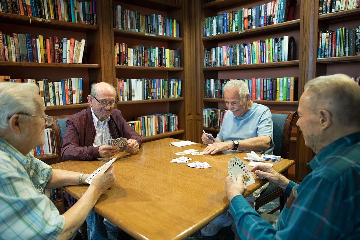 Senior gentleman sitting at a card table playing cards surrounded by bookshelves