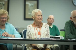 Senior men and women sitting at tables front facing in a classroom like setting