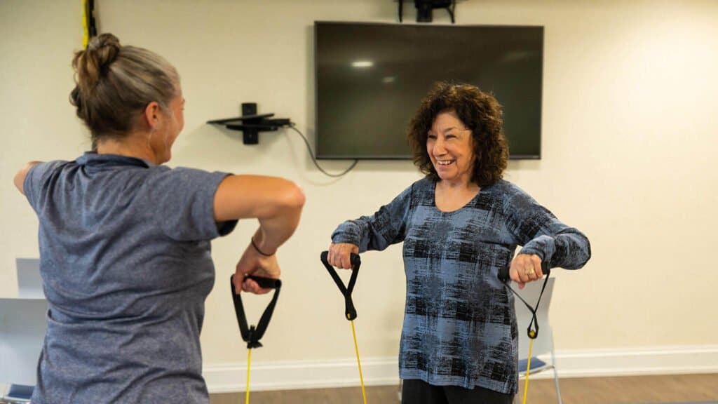 Two mature woman facing each other using workout bands to exercise