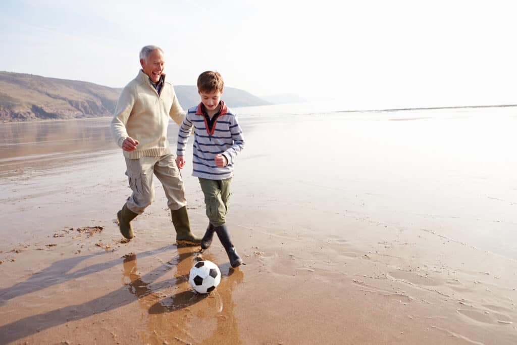 grandfather and grandson at beach kicking soccer ball