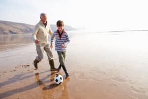 grandfather and grandson at beach kicking soccer ball