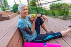 Older adult woman in workout clothes sitting & eating a healthy snack